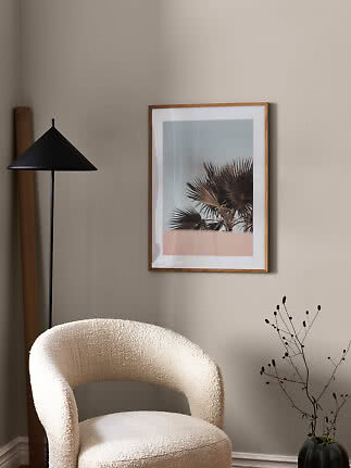 Moderne stuehjørne med cremefarvet lænestol, sort gulvlampe og indrammet palmeplakat