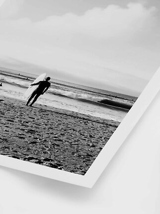 Foto in bianco e nero di un surfista con tavola sulla spiaggia vicino alle onde