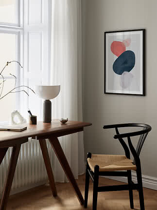 Gerahmter abstrakter Kunstdruck an der Wand über Holztisch und schwarzem Stuhl am Fenster