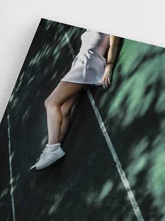 Woman in white dress and white sneakers lying on dark court with white lines
