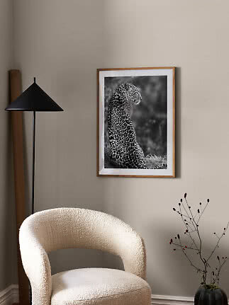 Indrammet sort-hvid leopardplakat på beige væg over en lys lænestol