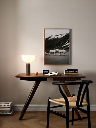 Bureau en bois avec chaise noire, lampe de table et photo encadrée sur mur beige