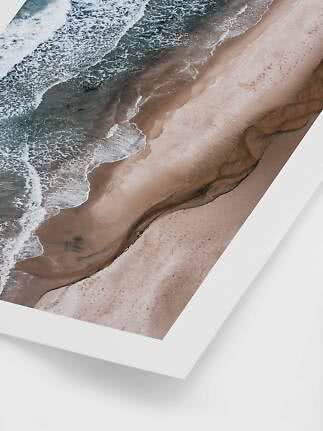 Angled aerial photo of waves meeting a sandy beach, shown as framed wall art