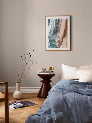 Bedroom with blue bedding, white pillows, and framed beach print on a beige wall