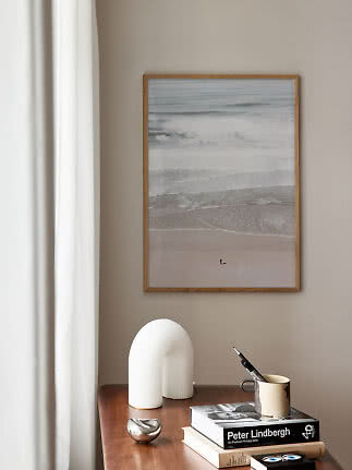 Gerahmter Stranddruck mit Wellen über einem Holztisch mit Büchern, Vase und Becher