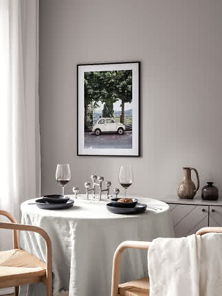 Dining area with round table, black plates, wine glasses, and framed photo of a small white car
