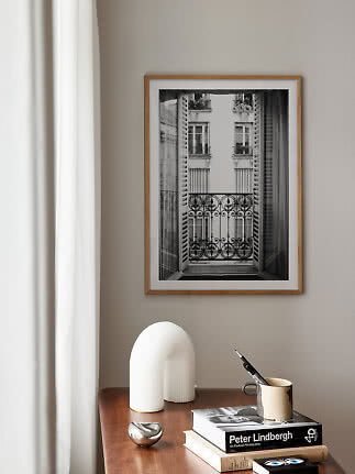 Framed black-and-white balcony photo on beige wall above wooden table with books and vase