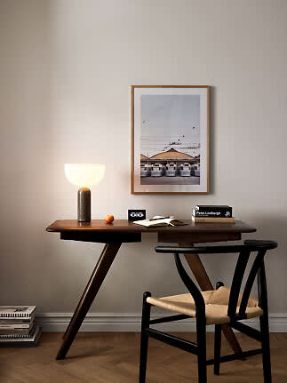 Dunkler Holzschreibtisch mit schwarzem Stuhl, leuchtender Tischlampe und gerahmtem Poster