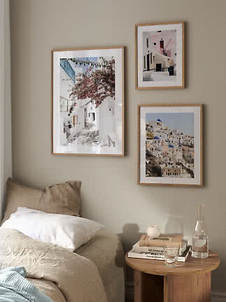 Three wooden framed travel prints hang above a bed beside a round bedside table.