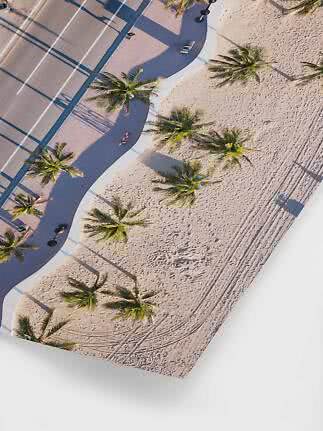 Aerial view of beach promenade with palm trees, sand, and road beside the shore