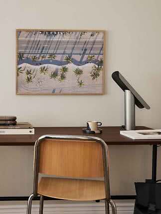 Home office with wooden chair, dark desk, and framed aerial photo of palm trees by a beach road