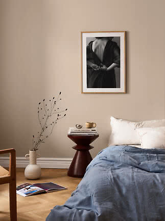 Ruhiges Schlafzimmer mit blauer Bettdecke, dunklem Beistelltisch, Vase und gerahmtem Schwarzweißbild