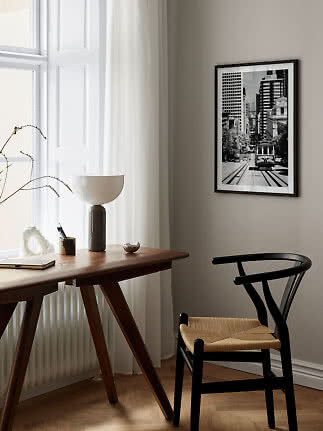 Black framed black-and-white city print hanging above a wooden desk in a bright modern room.