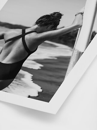 Black-and-white poster of woman in black swimsuit leaning on a surfboard at the beach