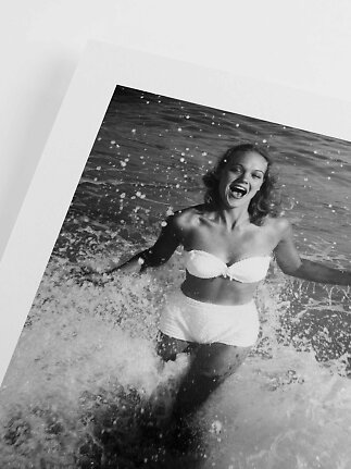 Sort-hvid foto af smilende kvinde i hvid bikini, der løber gennem havets bølger