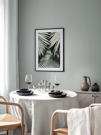 Framed palm leaf print above a set dining table in a bright Scandinavian-style room