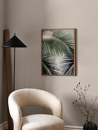 Indrammet plakat med grønne palmeblade på beige væg i moderne stue