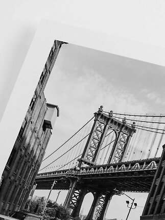 Sort-hvid plakat af Manhattan Bridge set nedefra mellem murstensbygninger