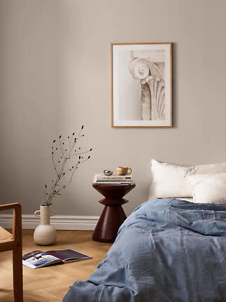Calm bedroom with blue bedding, round bedside table, vase, and framed wall art