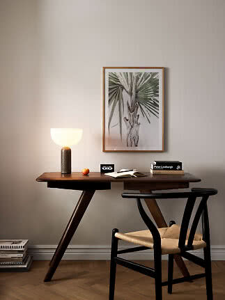 Donkerhouten bureau met brandende tafellamp, stoel en ingelijste palmprint aan de muur.