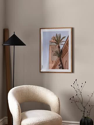 Framed photo print of a palm by a sand-colored building on a beige living room wall