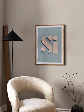 Gerahmtes typografisches "Si"-Poster an beigefarbener Wand über weißem Sessel neben schwarzer Stehlampe