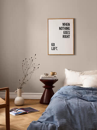 Indrammet typografiplakat med teksten "When nothing goes right go left" over en seng i soveværelse.