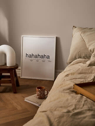 Poster tipografico incorniciato appoggiato al muro vicino al letto, lampada e tazza su un libro.