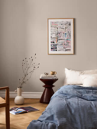 Schlafzimmer mit blauer Bettdecke, dunklem Beistelltisch und gerahmter Collage an beige Wand