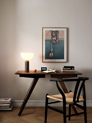 Dark wood desk with lit table lamp, chair, and framed photo on a beige wall.