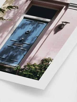 Blue front door in a pink facade with wall light and flowering plants below