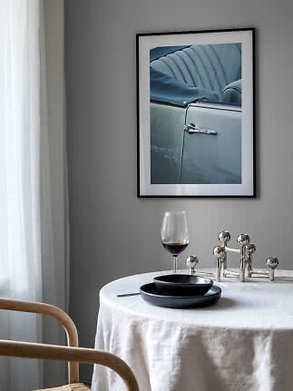 Gerahmtes Foto eines hellblauen Oldtimers über gedecktem Tisch mit Glas und schwarzen Tellern