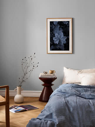Framed floral print on a gray wall above a bed with blue bedding and a small side table