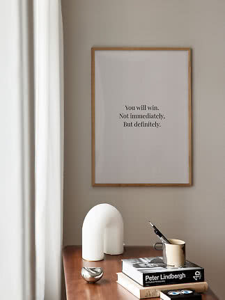Indrammet citatplakat på beige væg over træbord med bøger, krus og hvid skulptur