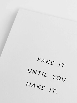 Biały minimalistyczny plakat z czarnym napisem: „FAKE IT UNTIL YOU MAKE IT.”