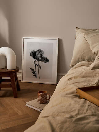 Camera da letto accogliente con biancheria beige, stampa floreale incorniciata e lampada bianca