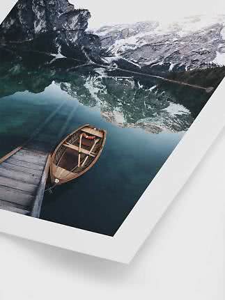 Wooden boat by a dock on a calm mountain lake with snowy peaks reflected in the water