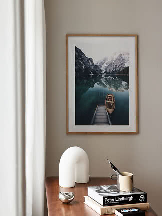 Framed mountain lake print with boat above a wooden table with books and decor