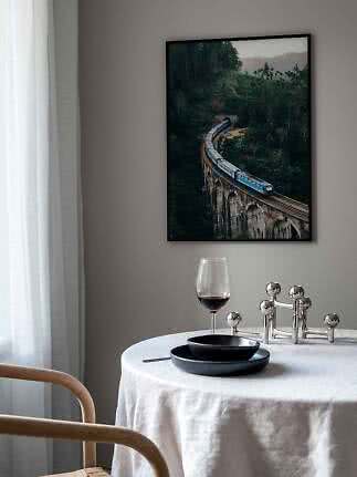 Indrammet plakat med blåt tog på buet viadukt i frodig skov over et dækket spisebord