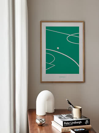 Poster verde incorniciato con campo da calcio astratto sopra un tavolo in legno con libri e decori