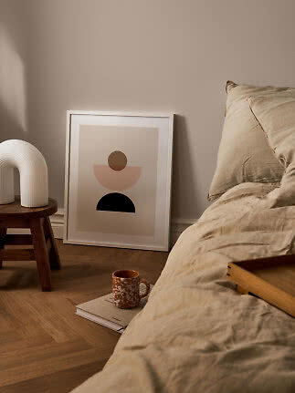 Minimalistisk soveværelse med beige sengetøj, abstrakt plakat, træskammel og hvid lampe.
