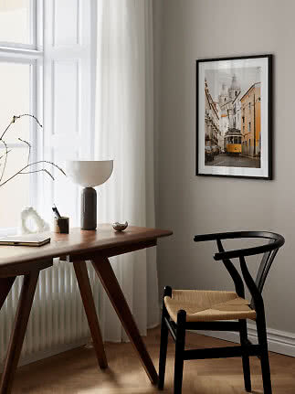 Gerahmter Stadtdruck mit gelber Straßenbahn an der Wand in einem hellen, minimalistischen Arbeitszimmer.