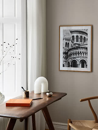 Framed black-and-white photo of a classical building on a beige wall above a wooden desk