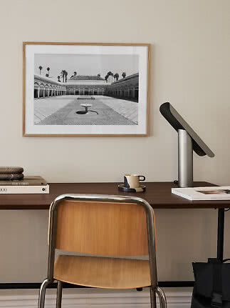 Home office with wooden chair, desk, black table lamp and framed black-and-white photo on wall