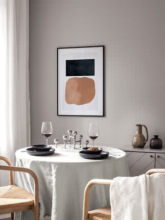 Minimalistische Essecke mit rundem Tisch, schwarzen Tellern, Weingläsern und abstrakter Wandkunst.