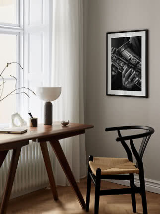 Indrammet sort-hvid foto af saxofon på væg over træskrivebord og sort stol