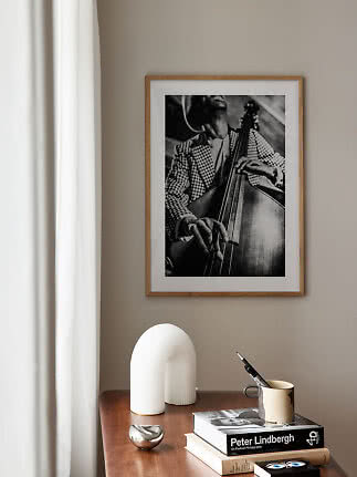 Photo noir et blanc encadrée d’un contrebassiste sur mur beige au-dessus d’une table en bois