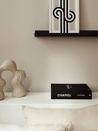 Sort CHANEL-bog på hvid overflade med beige skulptur og grafisk kunst på hylde.