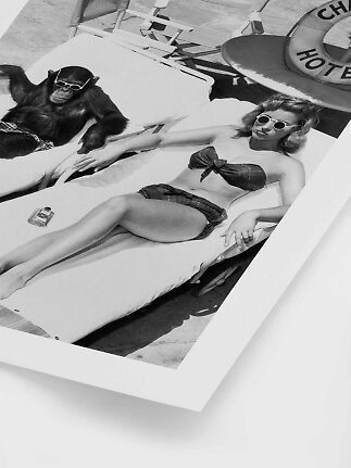 Black-and-white photo of a woman and chimpanzee in sunglasses on sun loungers by a pool