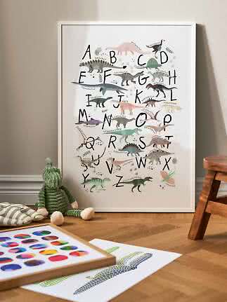 Framed dinosaur alphabet poster with colorful dinosaurs, leaning on the floor in a child's room